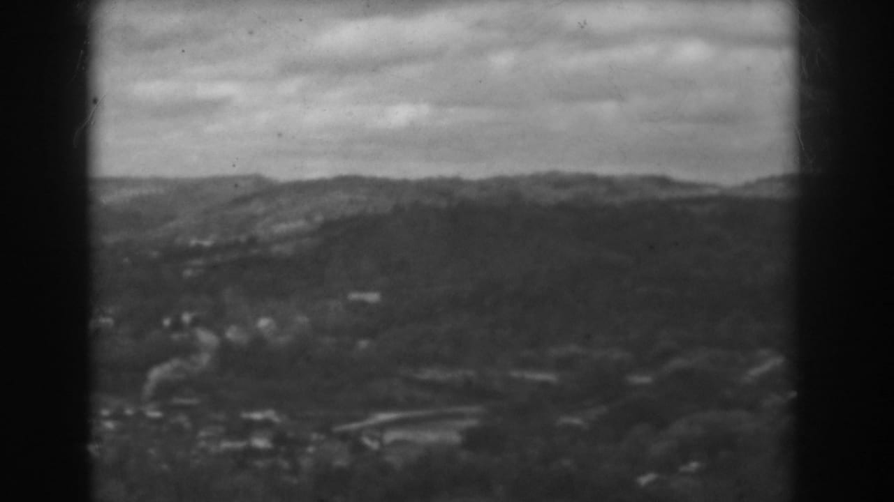 Soft black-and-white view of hills, rooftops, and an overcast sky.