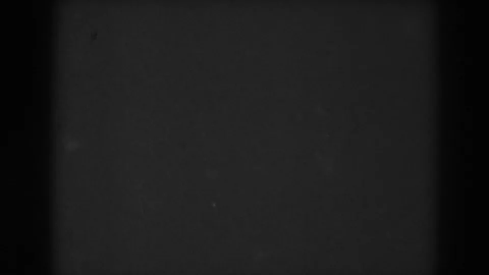 Darkened 8mm frame from the Vineland clip, with faint film grain and minimal visible landscape detail during the fade.