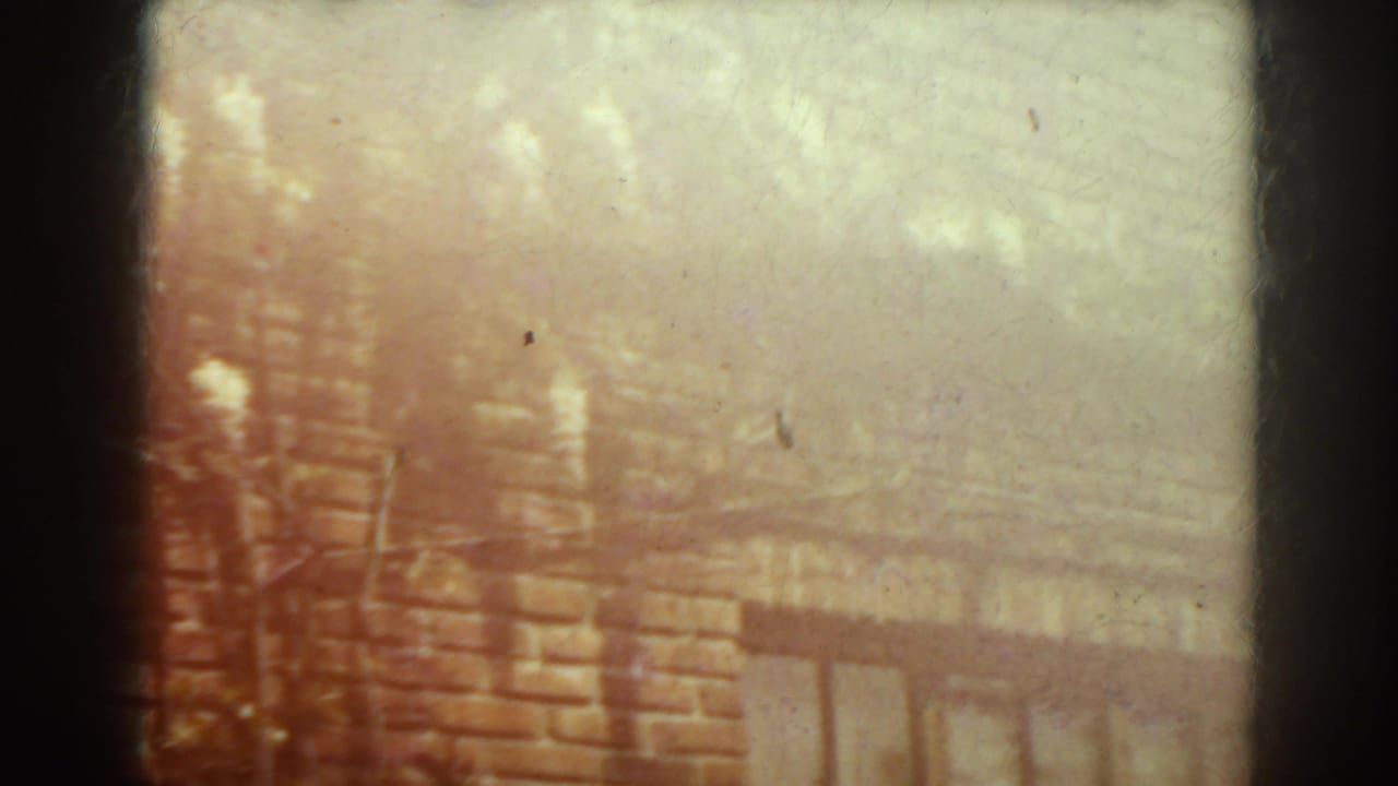 Overexposed 1938 West Virginia frame of a brick facade with barred window detail and diffuse tree-shadow patterns.