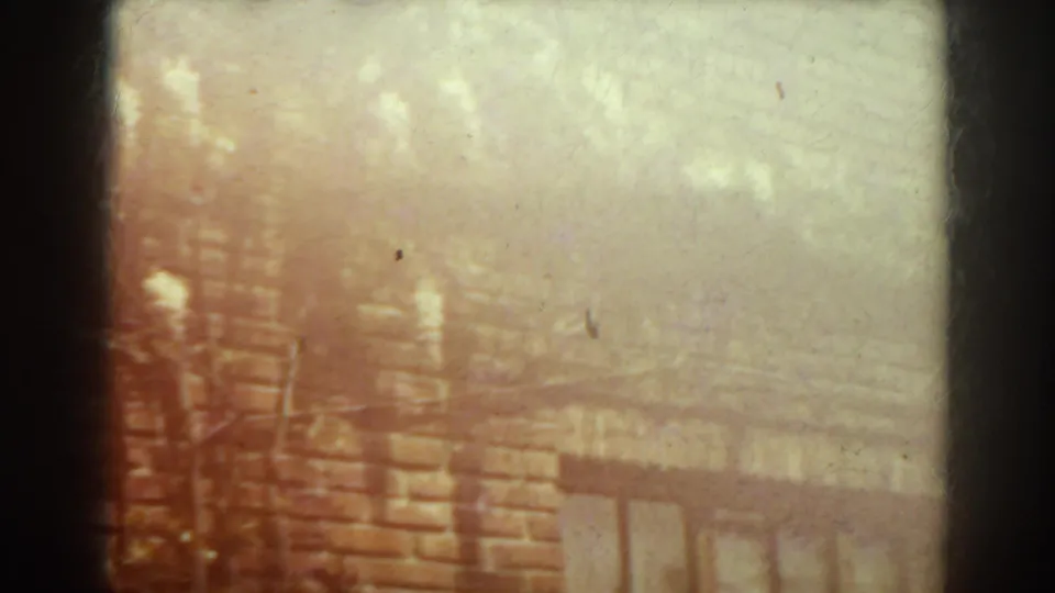 Overexposed 1938 West Virginia frame of a brick facade with barred window detail and diffuse tree-shadow patterns.