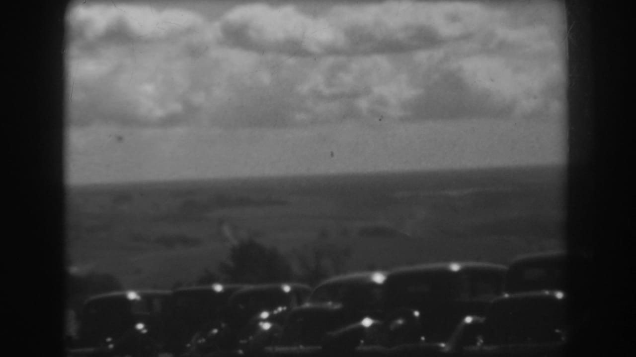 Cloudy rural landscape beyond a row of dark parked automobiles.