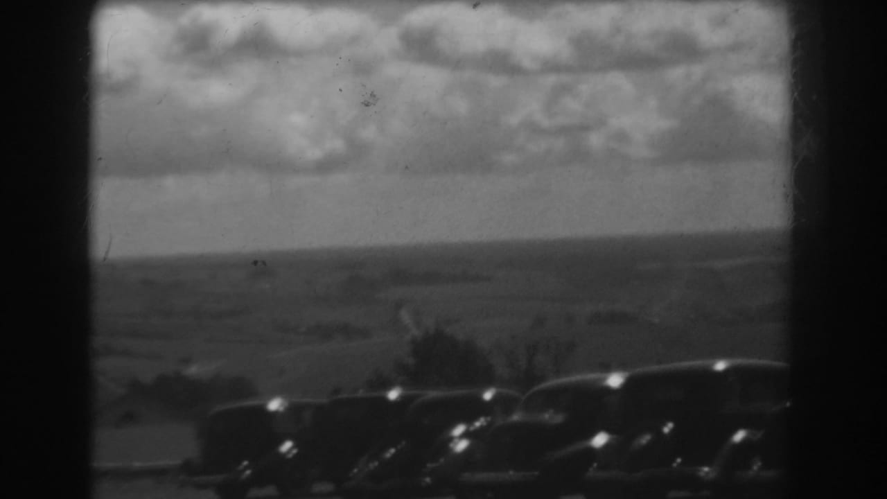 Parked cars silhouetted below a broad cloudy horizon.
