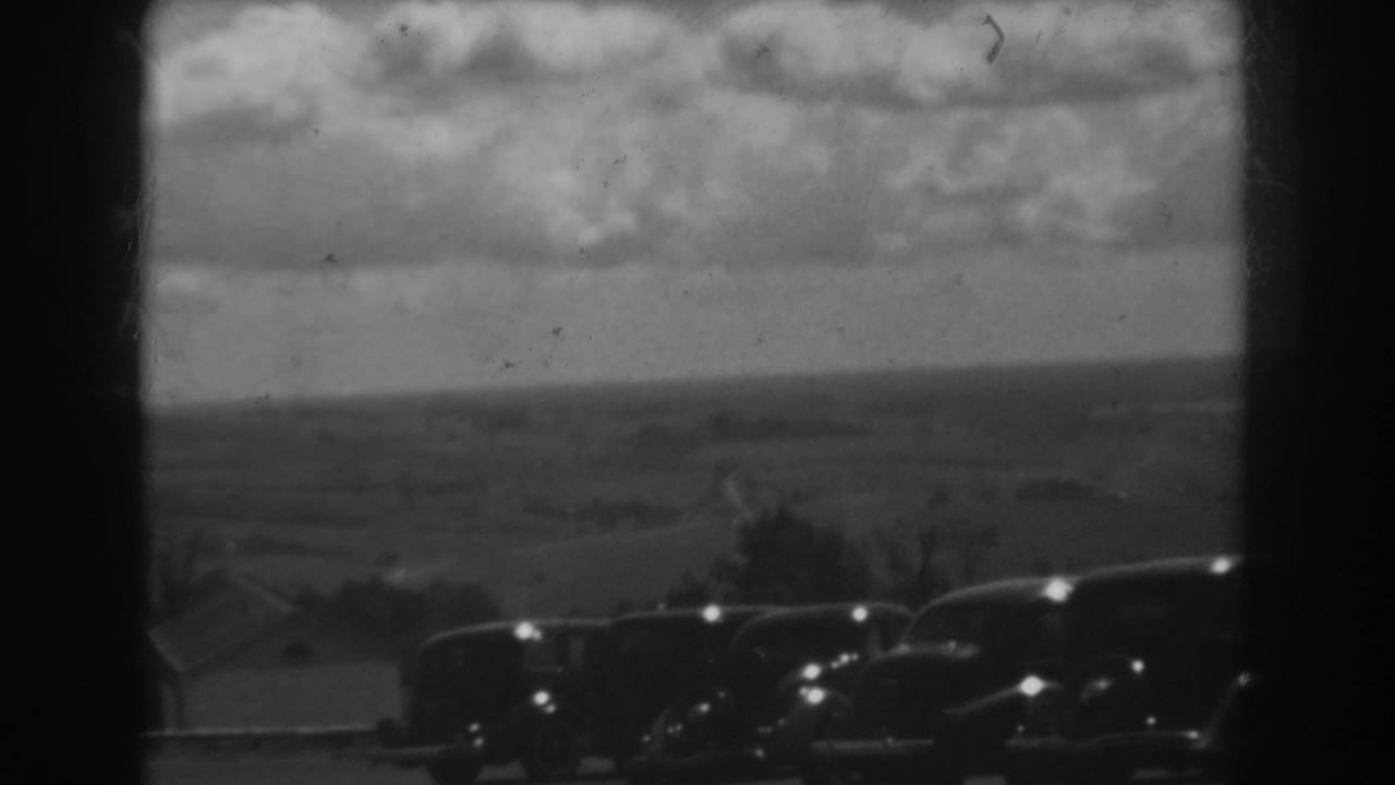 Black-and-white 8mm view of rural West Virginia with parked cars at the bottom edge and heavy clouds overhead.