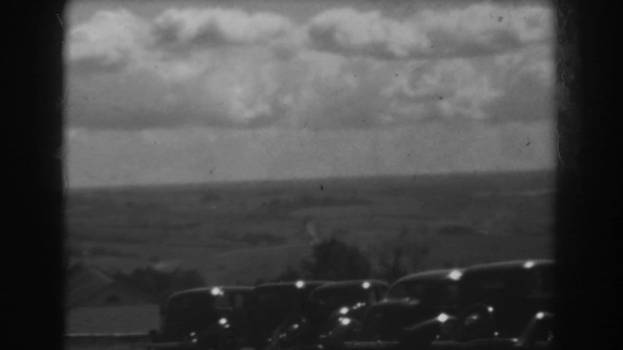 Final 1938 West Virginia frame showing dark parked cars, a distant countryside horizon, and textured cloud cover.