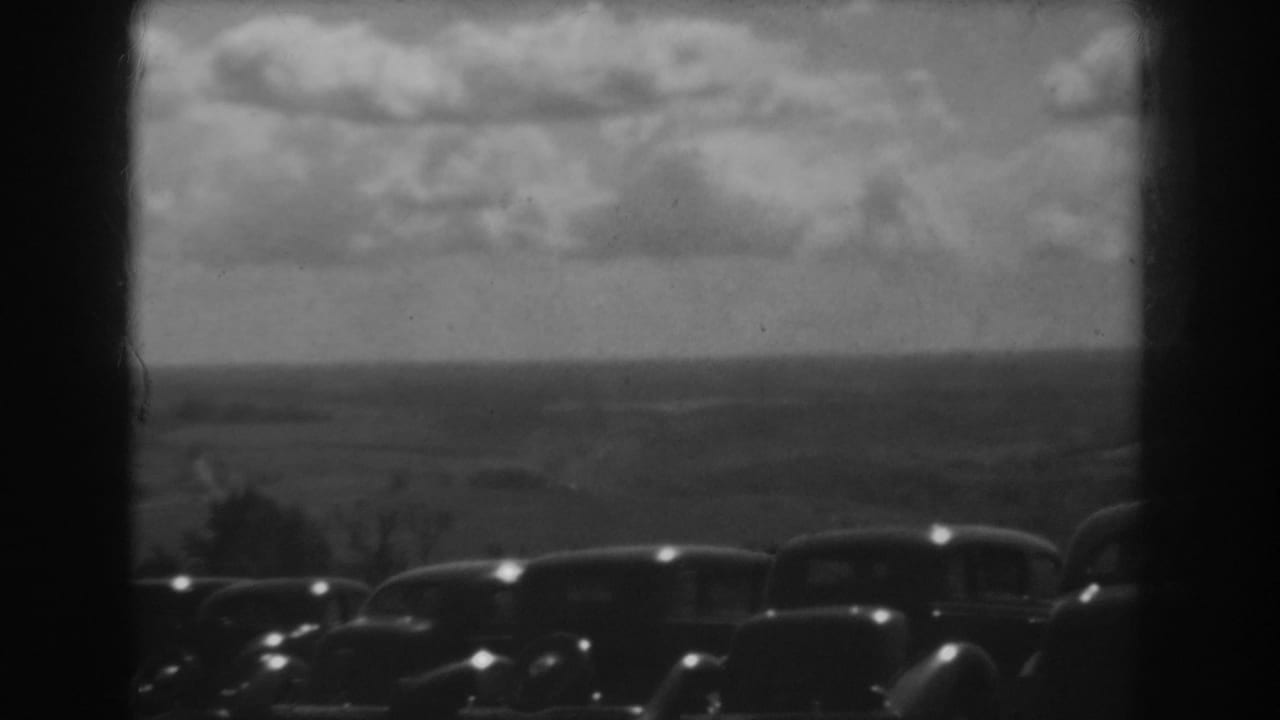 Row of parked cars on a hill with distant ridges and clouded sky.