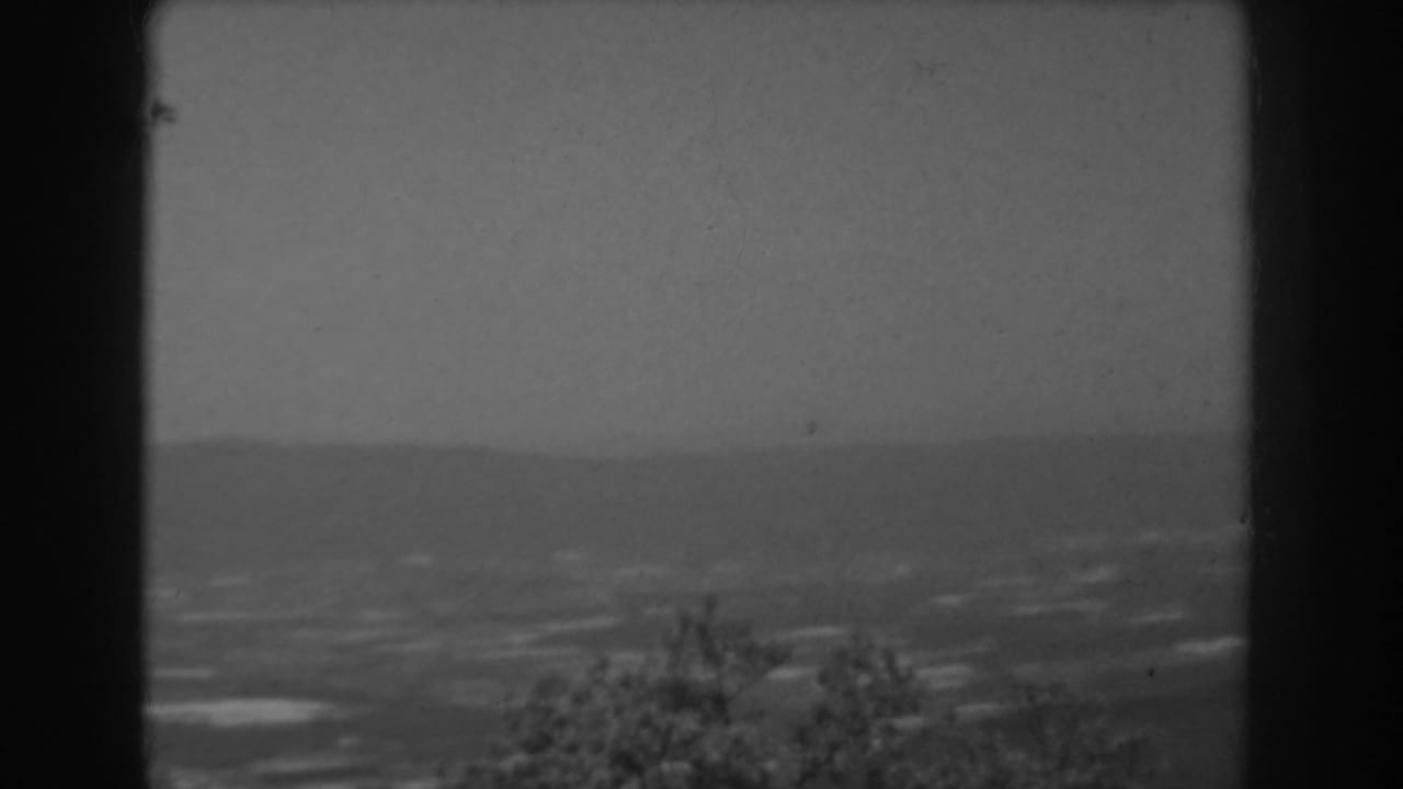 1938 West Virginia 8mm frame showing a hazy valley view through dark window framing, with distant hills and trees below.