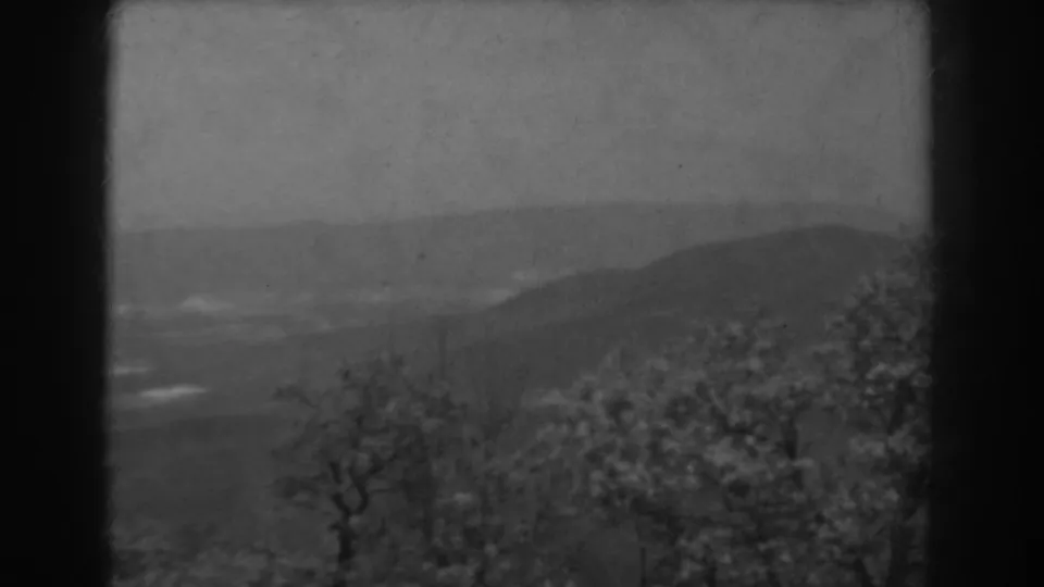 1938 West Virginia 8mm frame showing a soft-focus foggy valley, wooded foreground, distant hills, and a dark central film divider.