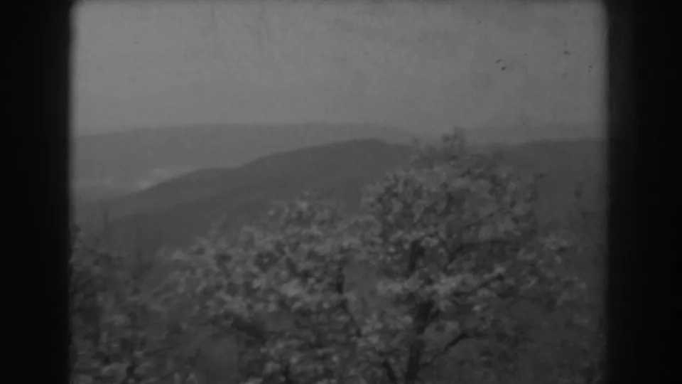 1938 West Virginia 8mm frame showing blossoming foreground trees and layered mountain ridges in soft cloudy light.