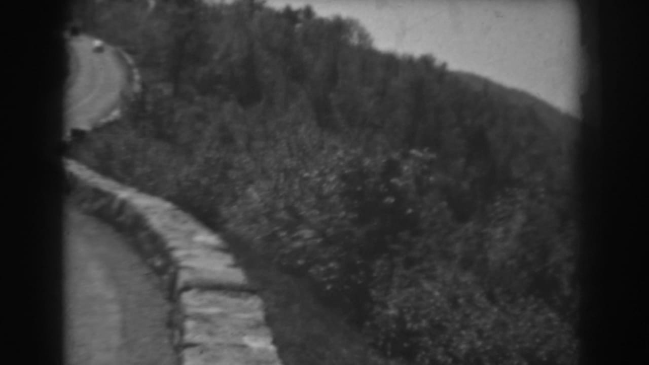 1938 West Virginia home-movie view of a winding road bordered by stonework and dense hillside vegetation.