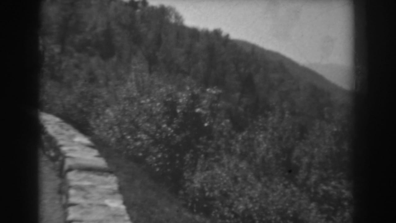 West Virginia 1938 8mm frame of a mountain road, stone border, wooded slope, and hazy distant hills.