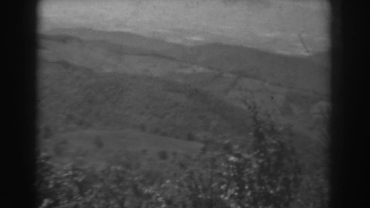 1938 West Virginia home-movie frame showing distant hills, open fields, and dark foreground trees in soft black-and-white.