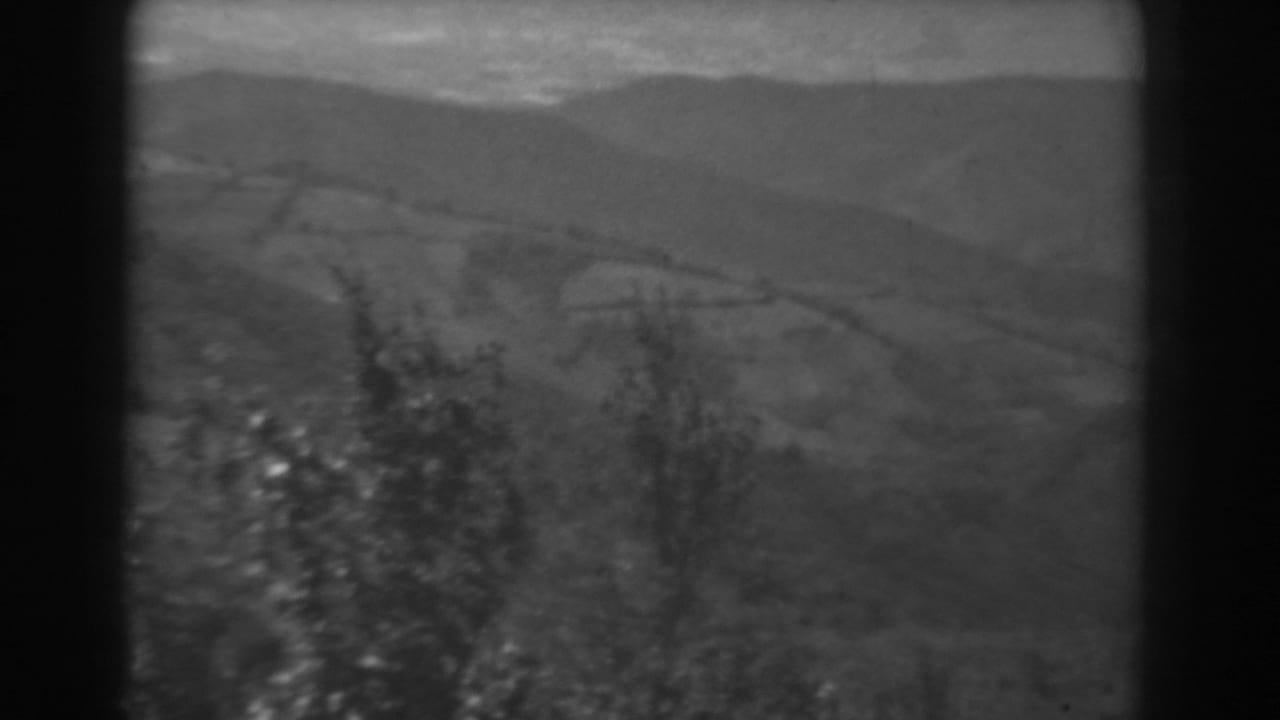 West Virginia 1938 home-movie frame with open fields, low hills, and dark tree shapes along the foreground edge.