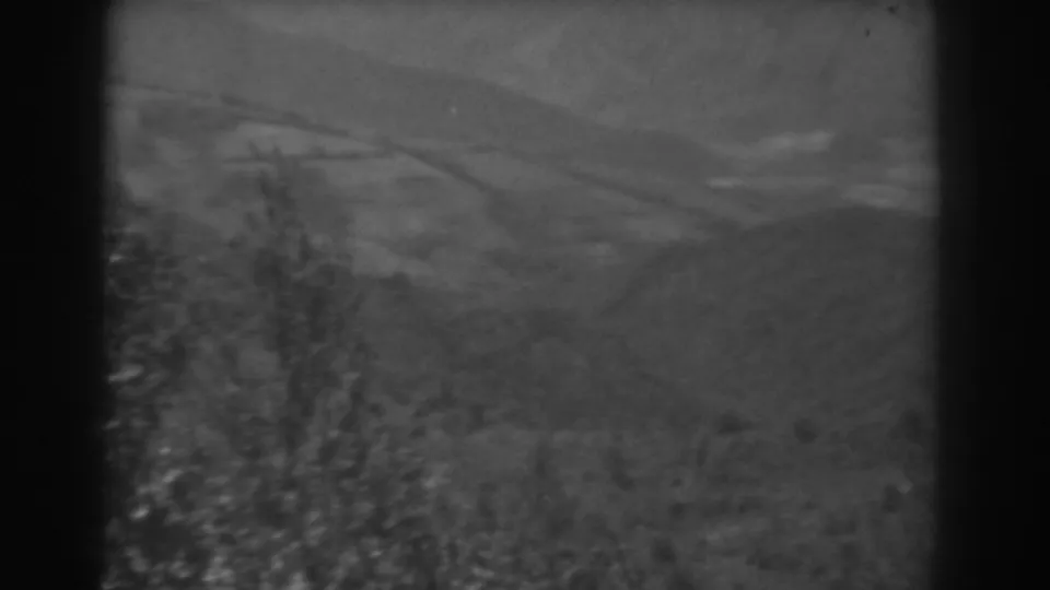 1938 West Virginia 8mm frame showing rural hills and fields with blurred foreground vegetation and visible film borders.