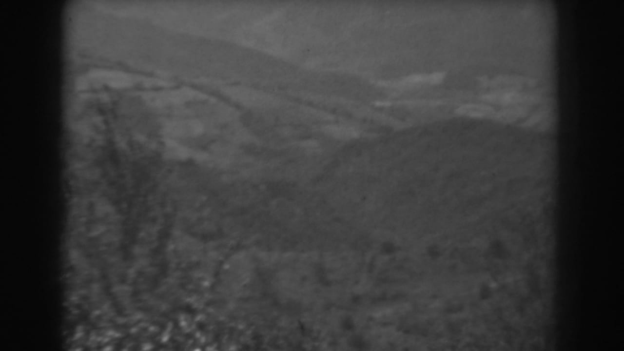 1938 West Virginia 8mm frame showing soft distant hills, a grassy foreground, brush, and a pale sky within dark film borders.
