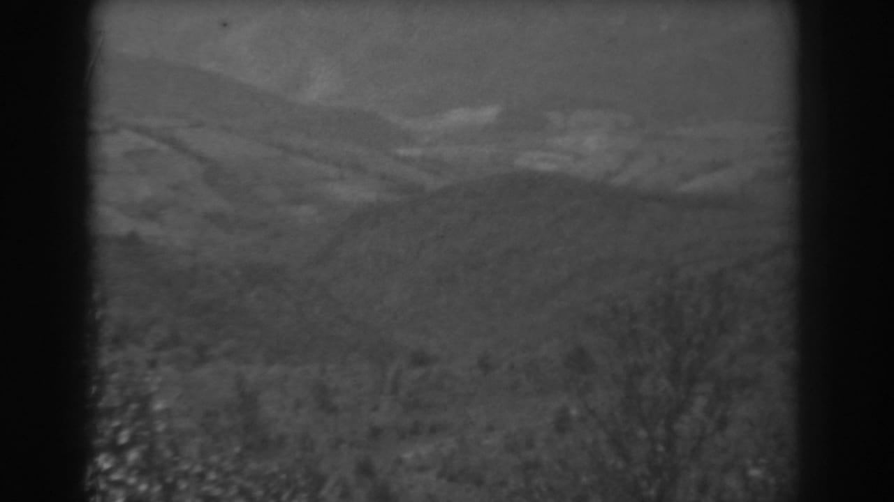 Soft monochrome hillside view with grass, brush, and distant ridges.