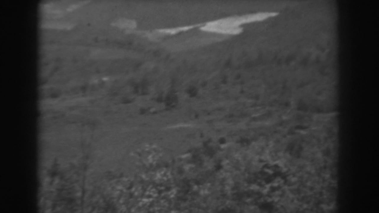 Black-and-white 8mm West Virginia landscape showing a grassy rural slope, brush, distant hills, and a bright diagonal midground area.
