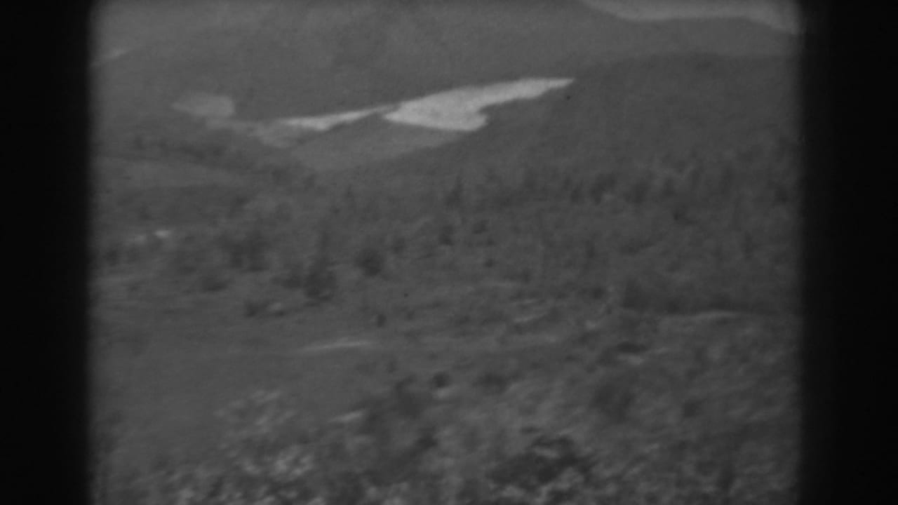 Monochrome view of wooded hills, distant ridges, and a pale winding waterway.