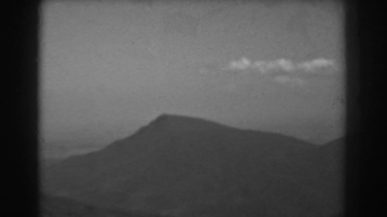 Soft black-and-white mountain silhouette below a clear sky with small clouds.
