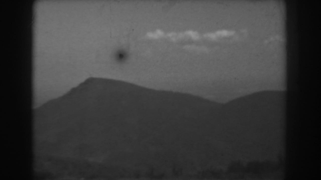 1938 West Virginia 8mm frame showing layered hills and a mountain ridge below scattered clouds, with visible film grain and marks.