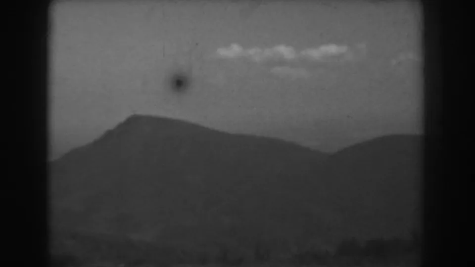 1938 West Virginia 8mm frame showing layered hills and a mountain ridge below scattered clouds, with visible film grain and marks.