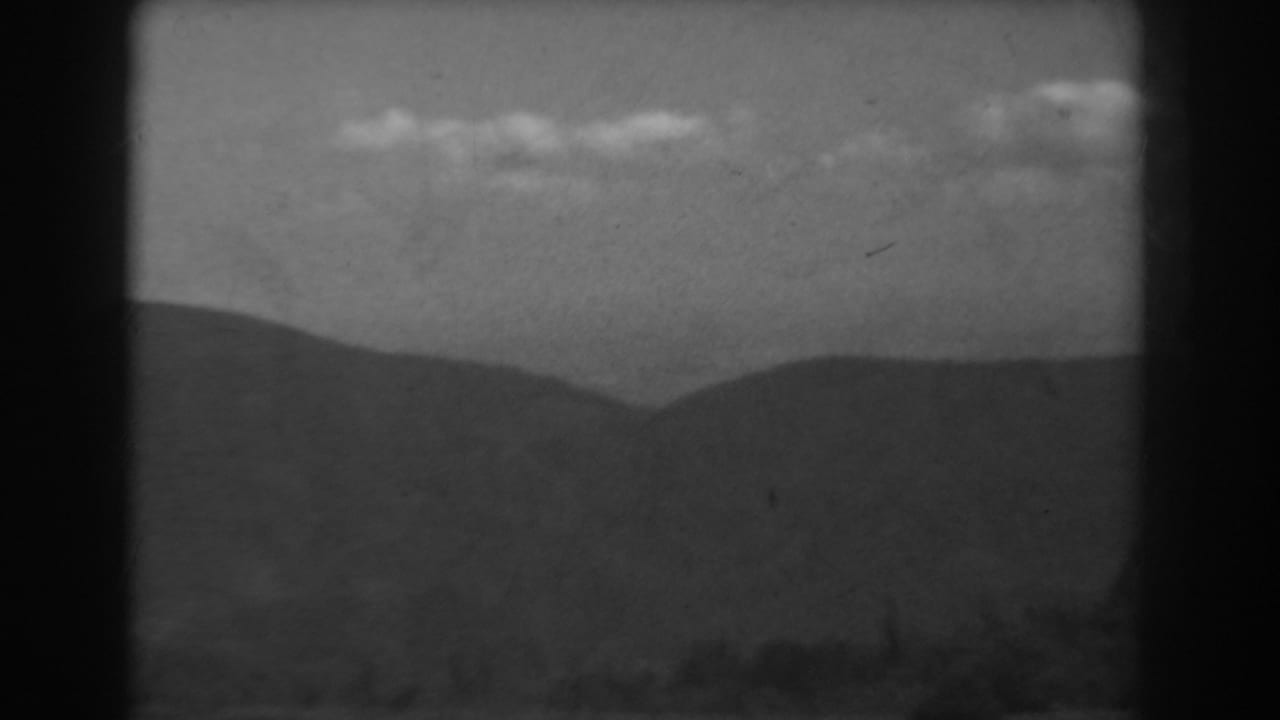1938 West Virginia 8mm frame with low overlapping ridges, a broad sky, and small bright clouds near the horizon.