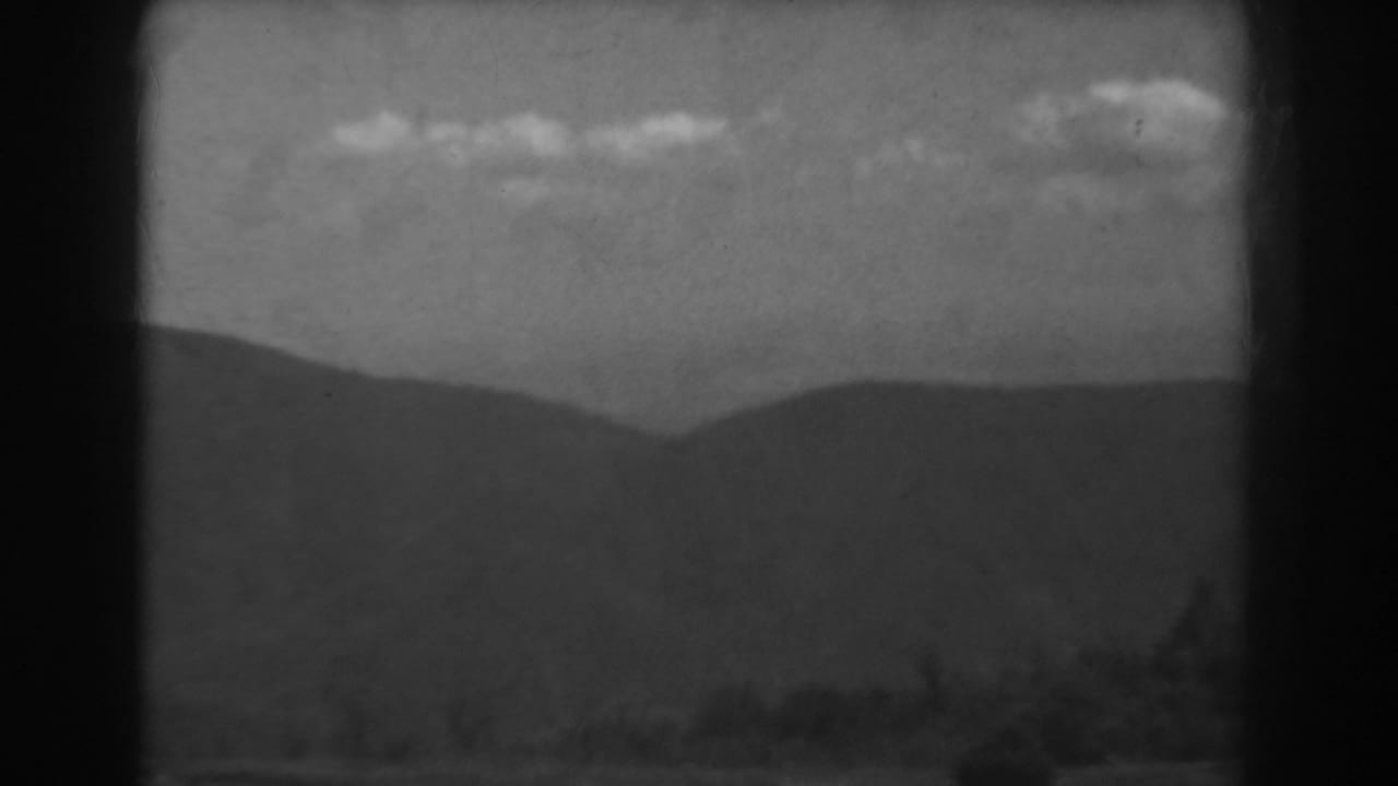 1938 West Virginia 8mm frame showing layered mountains, scattered clouds and a dark forested foreground.