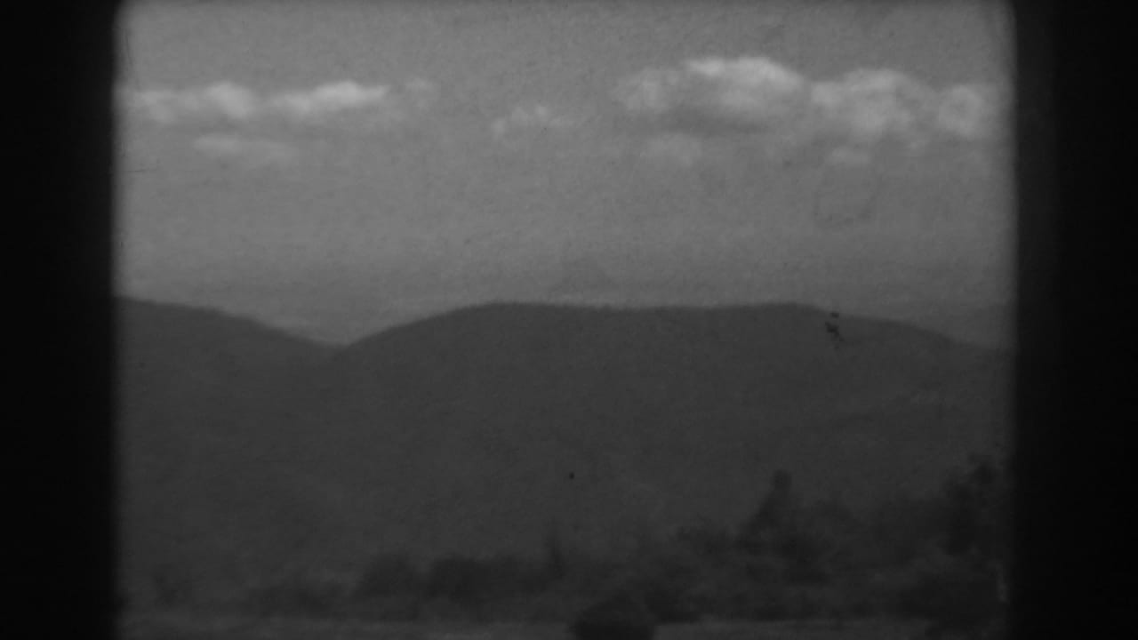 Rolling mountain silhouette under a lightly clouded sky with dark frame edges.