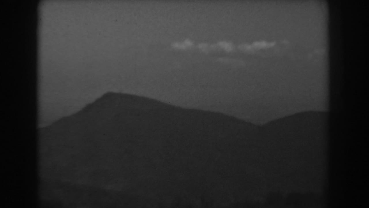 1938 8mm view of West Virginia hills, a dark foreground slope and soft clouds in a hazy sky.