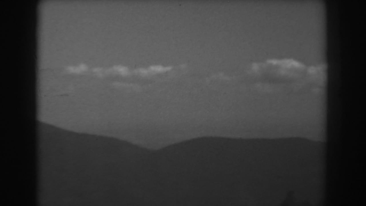 Clouds above distant mountain ridges in a black-and-white 8mm frame.