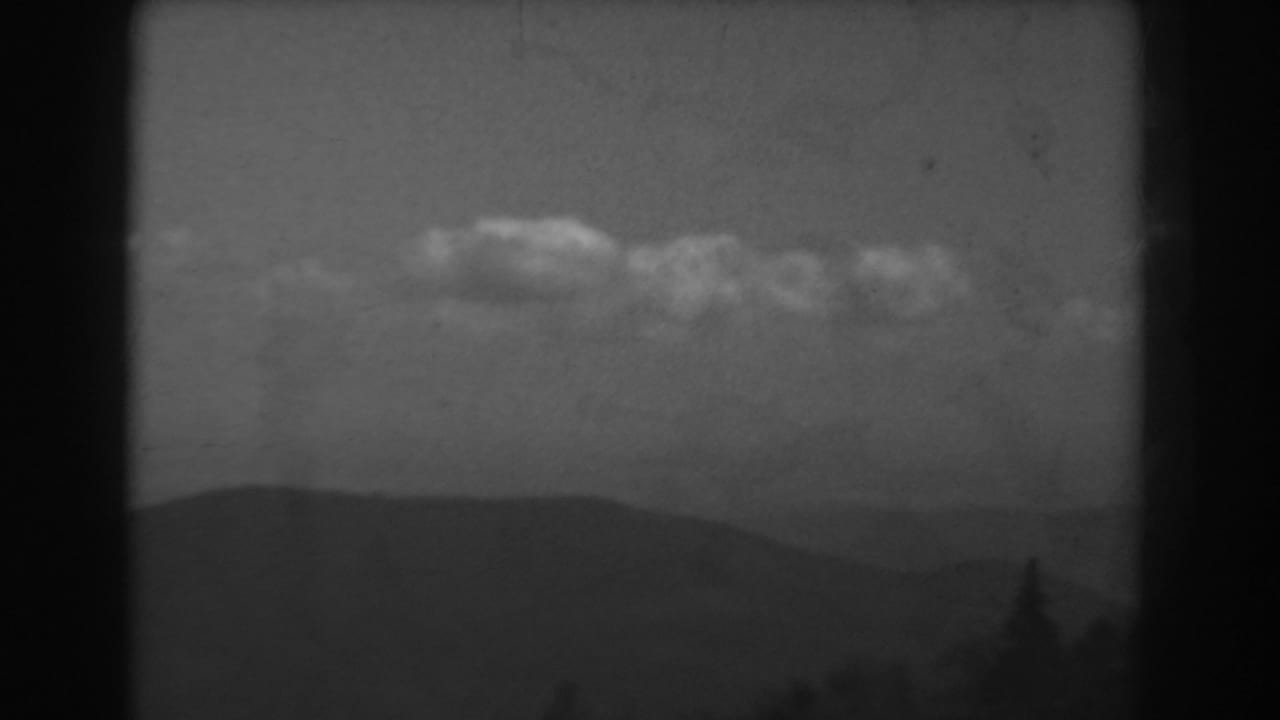 West Virginia 8mm landscape frame showing clouds, a low ridge, haze, and a dark treetop silhouette near the lower edge.