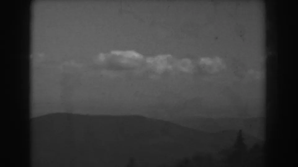 West Virginia 8mm landscape frame showing clouds, a low ridge, haze, and a dark treetop silhouette near the lower edge.