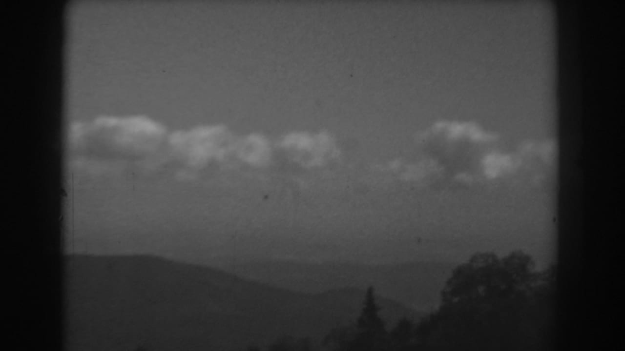 Black-and-white 1938 West Virginia frame showing a hazy mountain valley, cloud band, and dark trees along the lower edge.