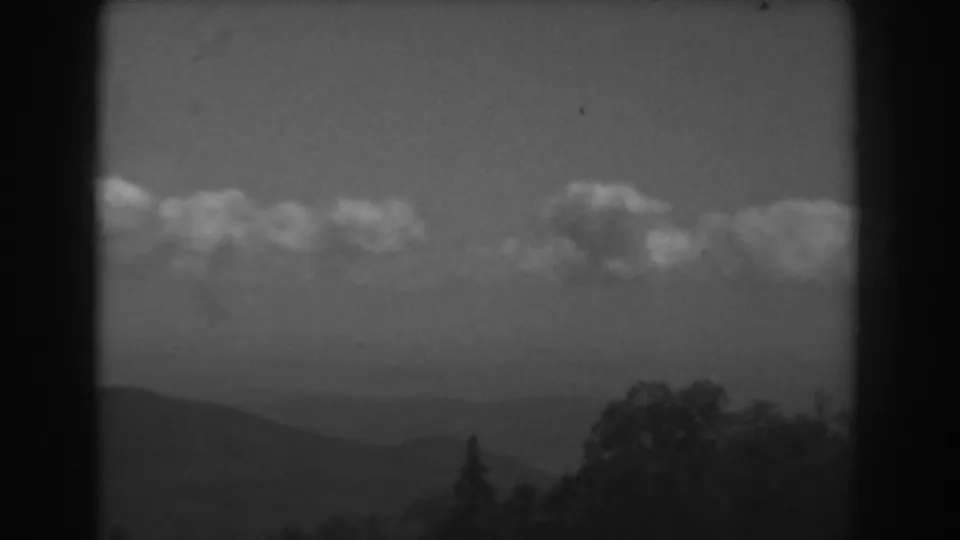 1938 West Virginia home-movie frame showing hazy hills, dark trees, and a horizontal cloud band across the sky.