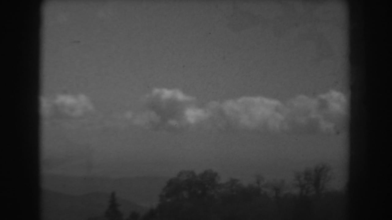 Black-and-white 8mm view of the West Virginia horizon with soft clouds, distant hills, and trees along the lower edge.