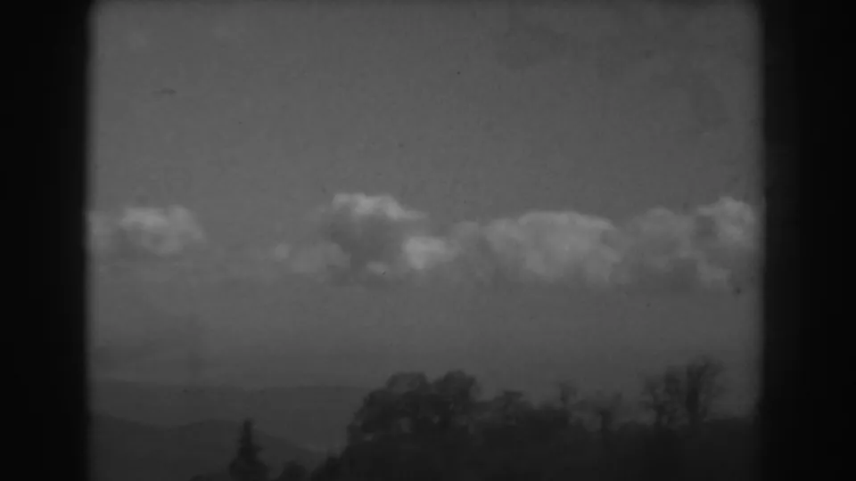 Black-and-white 8mm view of the West Virginia horizon with soft clouds, distant hills, and trees along the lower edge.