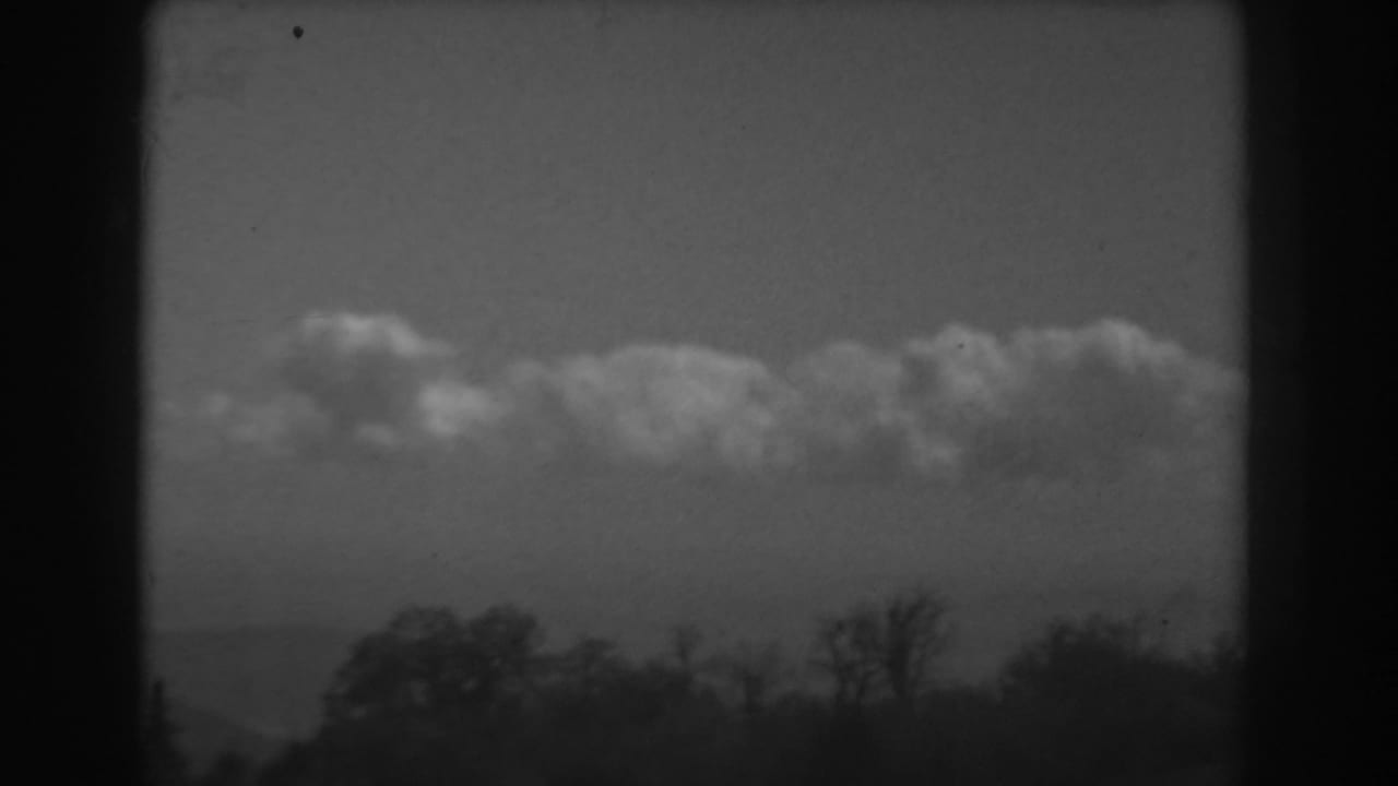 1938 West Virginia landscape frame with a low tree line, hazy ridge, and thick cloud bank in black-and-white 8mm texture.
