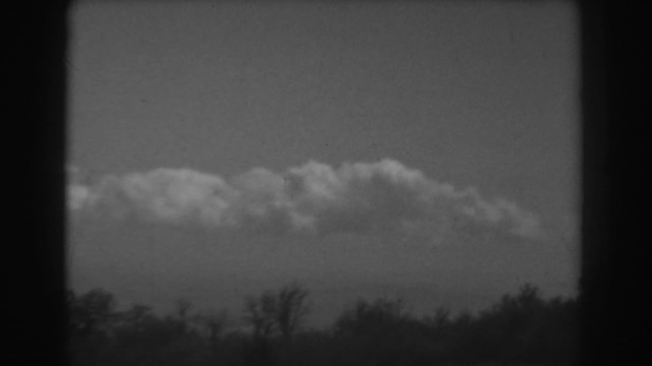 West Virginia home-movie still from 1938 showing a cloud bank above dark trees and a faint ridge line near the horizon.
