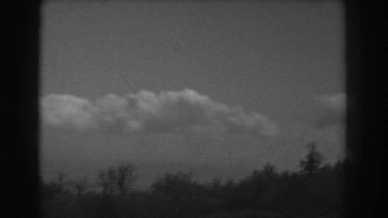 Fair-weather clouds above a dark treeline in a black-and-white film frame.