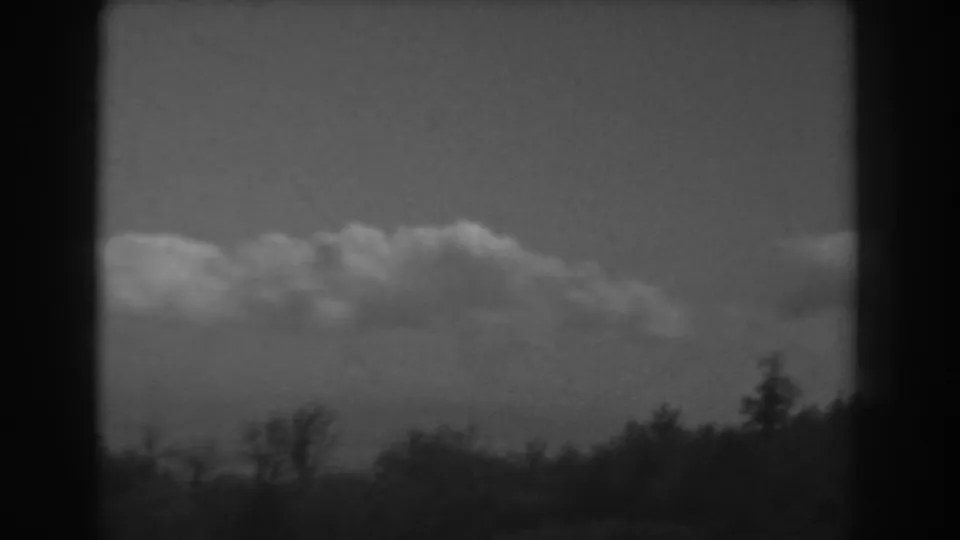 1938 West Virginia home-movie frame showing cumulus clouds over a dark wooded horizon.