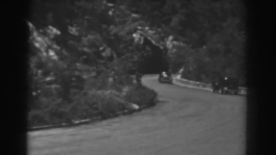 Black-and-white 8mm frame of cars traveling along a curvy West Virginia mountain road in 1938.