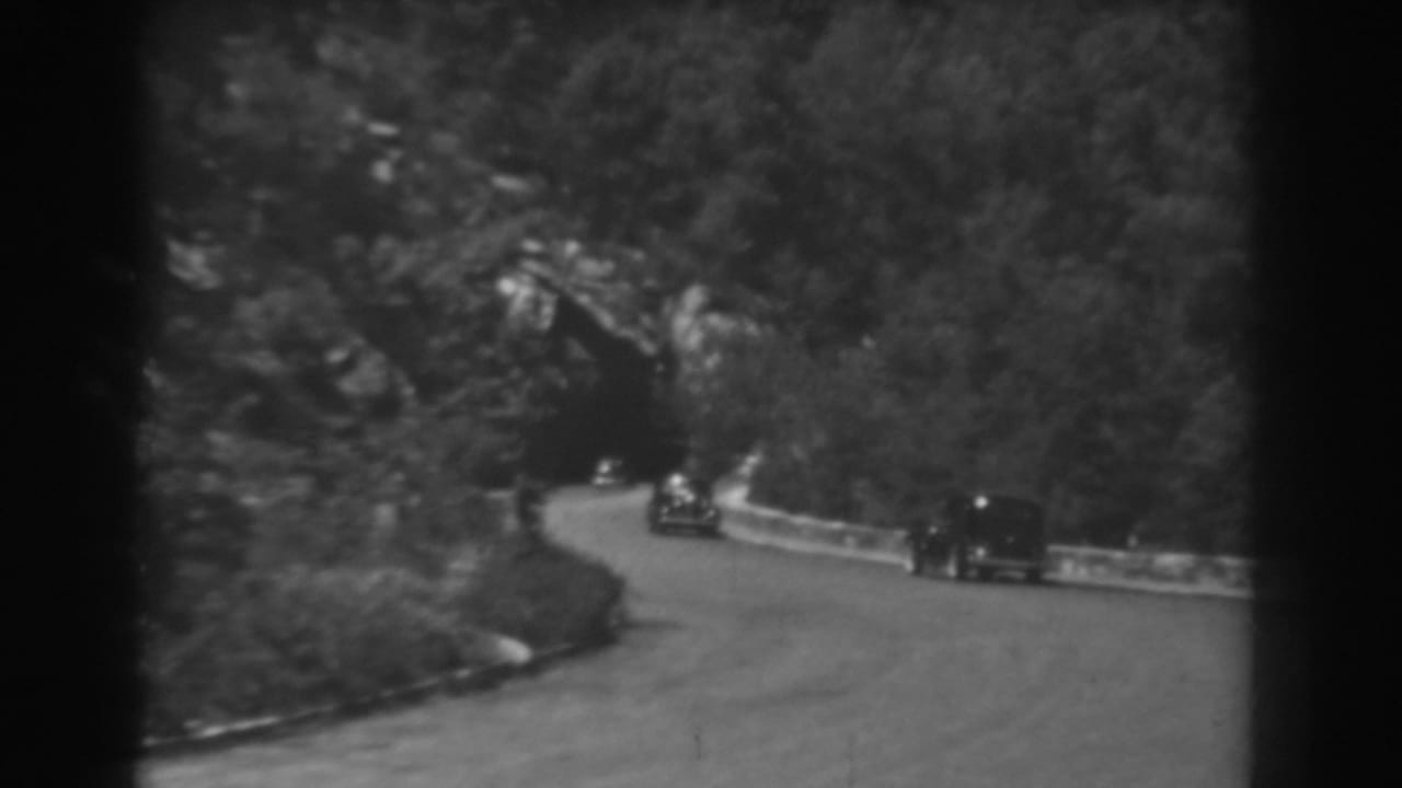 Cars continue along a curve beside a low wall near a tunnel entrance.