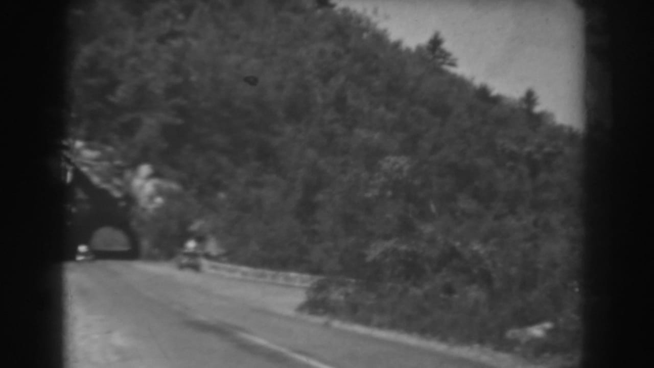 A small car moves along a curving West Virginia road after leaving a tree-covered tunnel in 1938 home-movie footage.