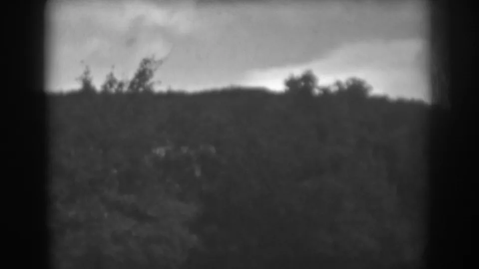 Soft 1938 8mm frame showing a rural hillside or ridge, shrubs, and a cloudy sky in Winchester, Maryland metadata.