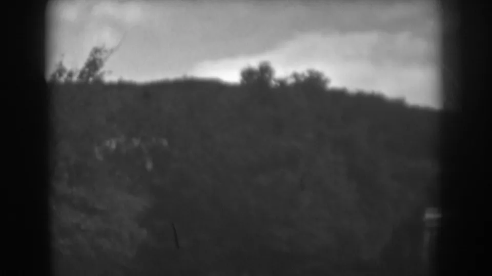 Winchester, Maryland home-movie frame with a dark ridge, trees, cloudy sky, and a faint small structure-like form at right.