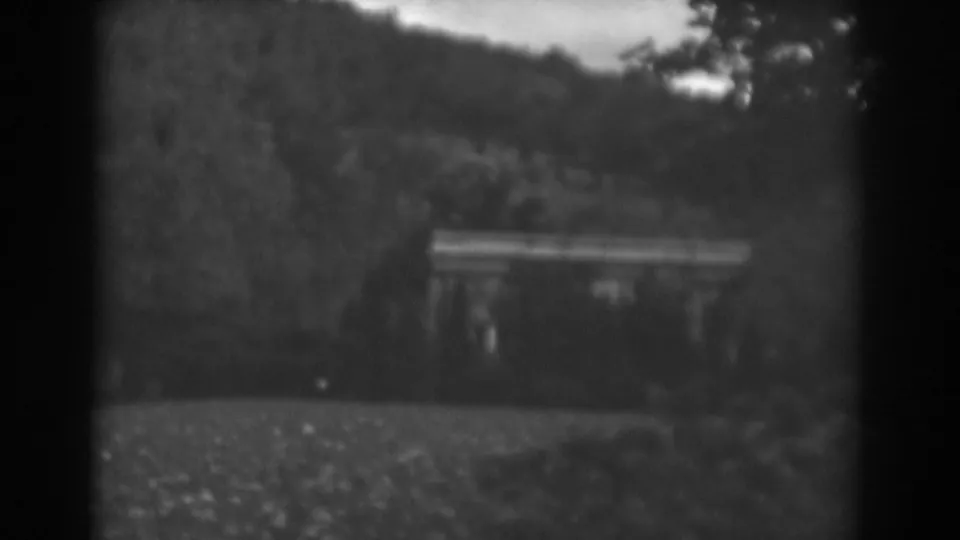 Winchester, Maryland 8mm frame from 1938 showing a small building or porch area among trees below a wooded hillside.