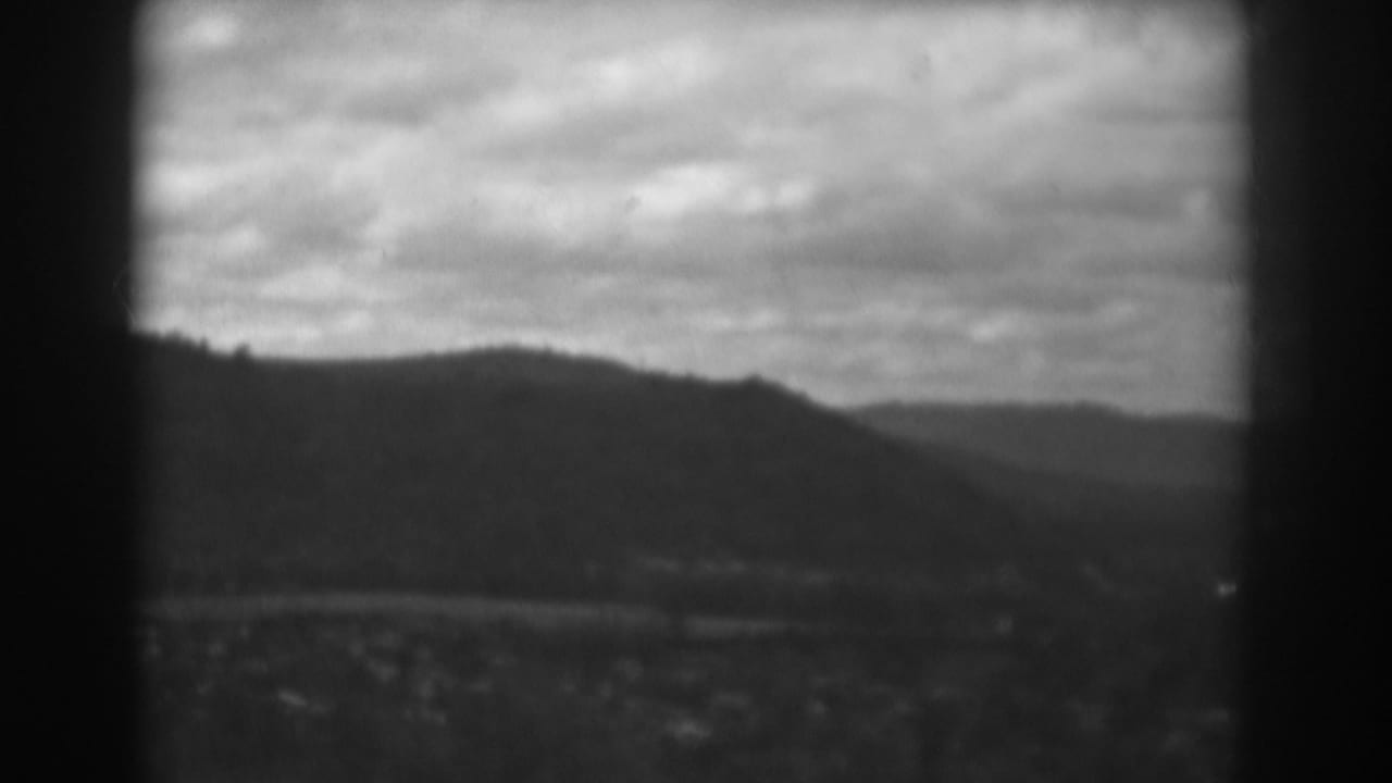 Black-and-white mountain ridge under cloudy sky with valley below.