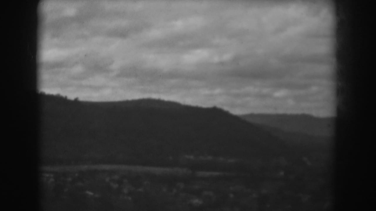 Black-and-white 8mm frame from the Winchester, Maryland clip with layered hills, cloudy sky, and faint buildings in the valley.