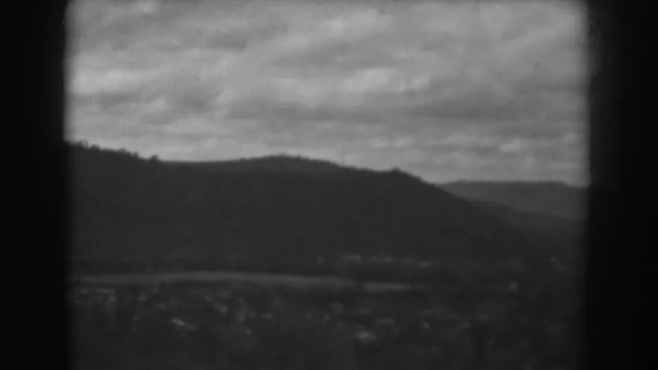 1938 home-movie frame near Winchester, Maryland, with a dark hill profile, overcast sky, and blurred valley details below.