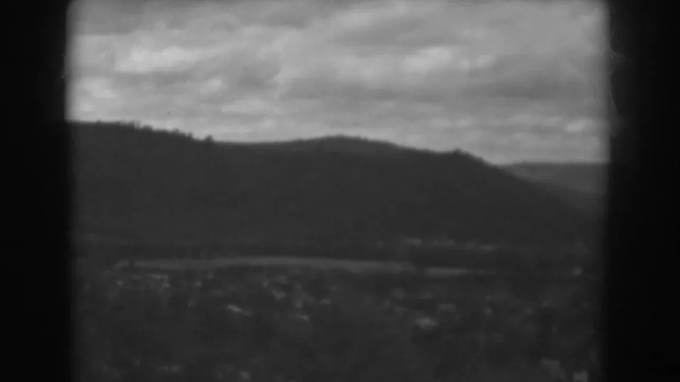 Black-and-white 8mm view near Winchester, Maryland, showing a rounded ridge, cloudy sky, and indistinct town structures in the valley.