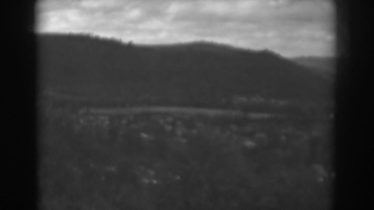 1938 Winchester, Maryland view with a dark vertical frame edge dividing mountains, cloudy sky, a distant road, and small buildings.